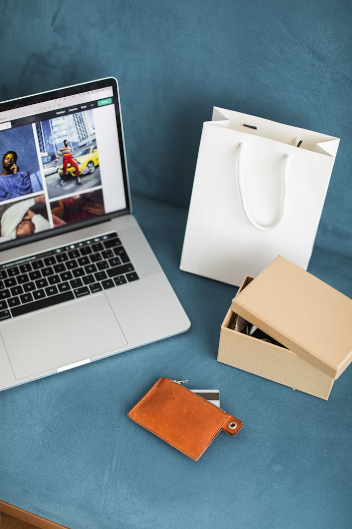 A high-angle view of online shopping items including a laptop, gift bags, and wallet on a blue surface.