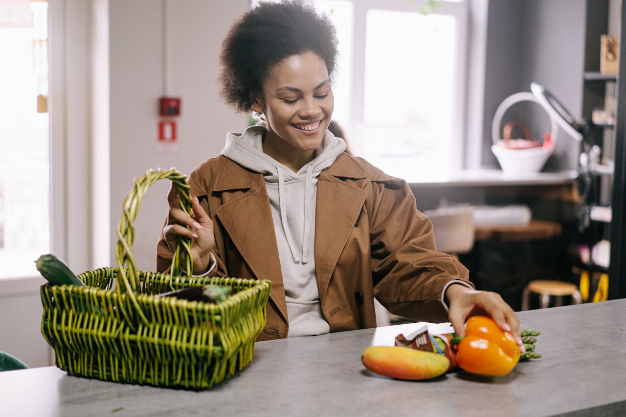 A woman joyfully choosing fruits and vegetables while grocery shopping indoors with a green basket.